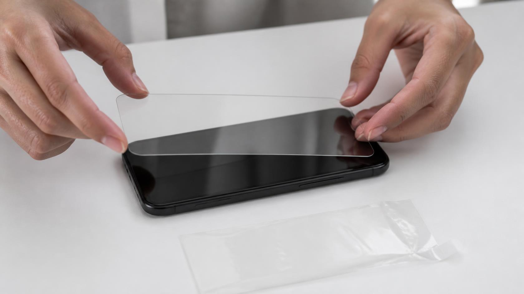 Panzerglas wird auf ein Smartphone-Display aufgebracht, daneben eine Schutzfolie